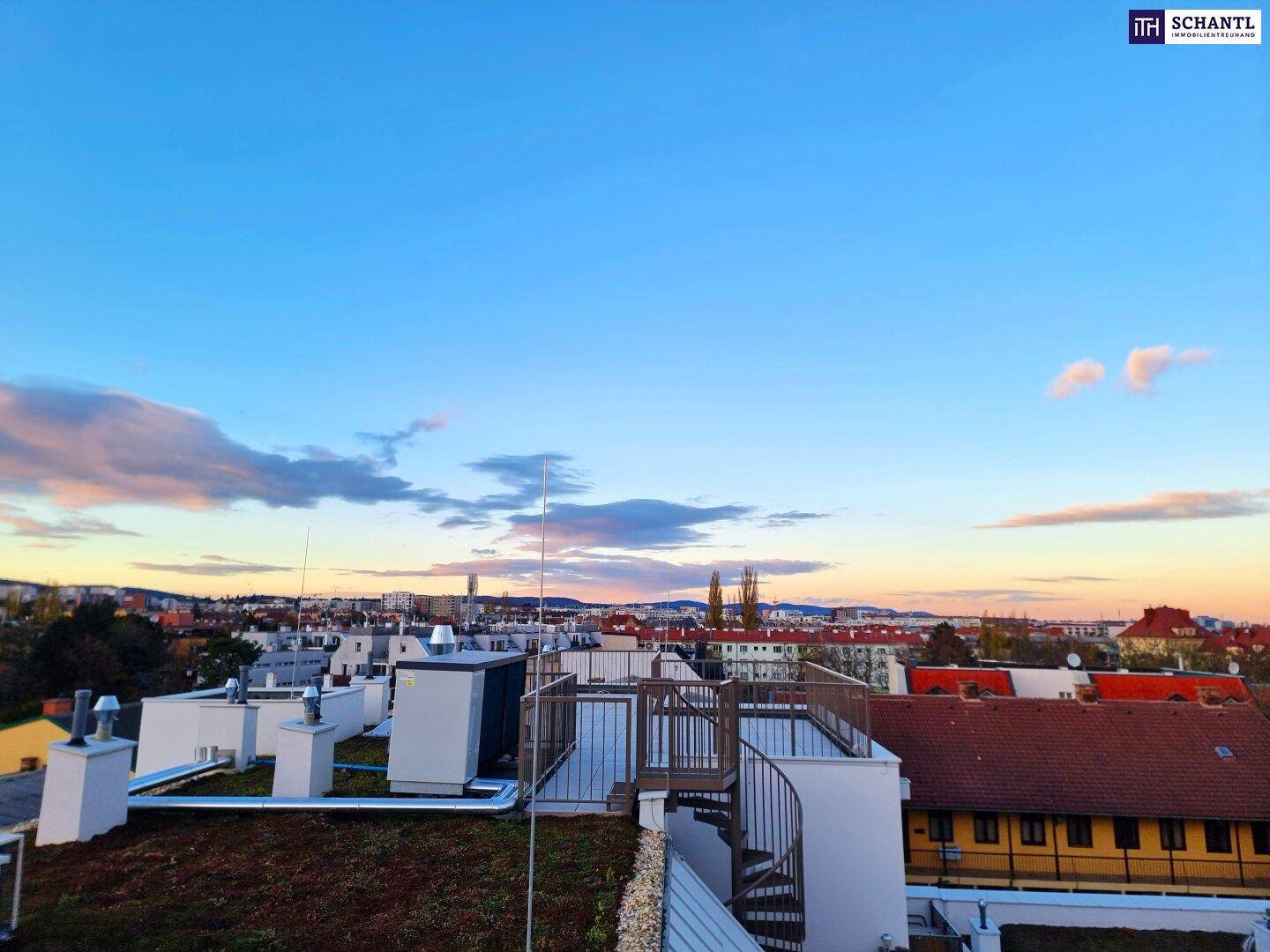 Panoramablick über die Stadt bei Sonnenuntergang mit Bergen im Hintergrund und Wohngebäuden.