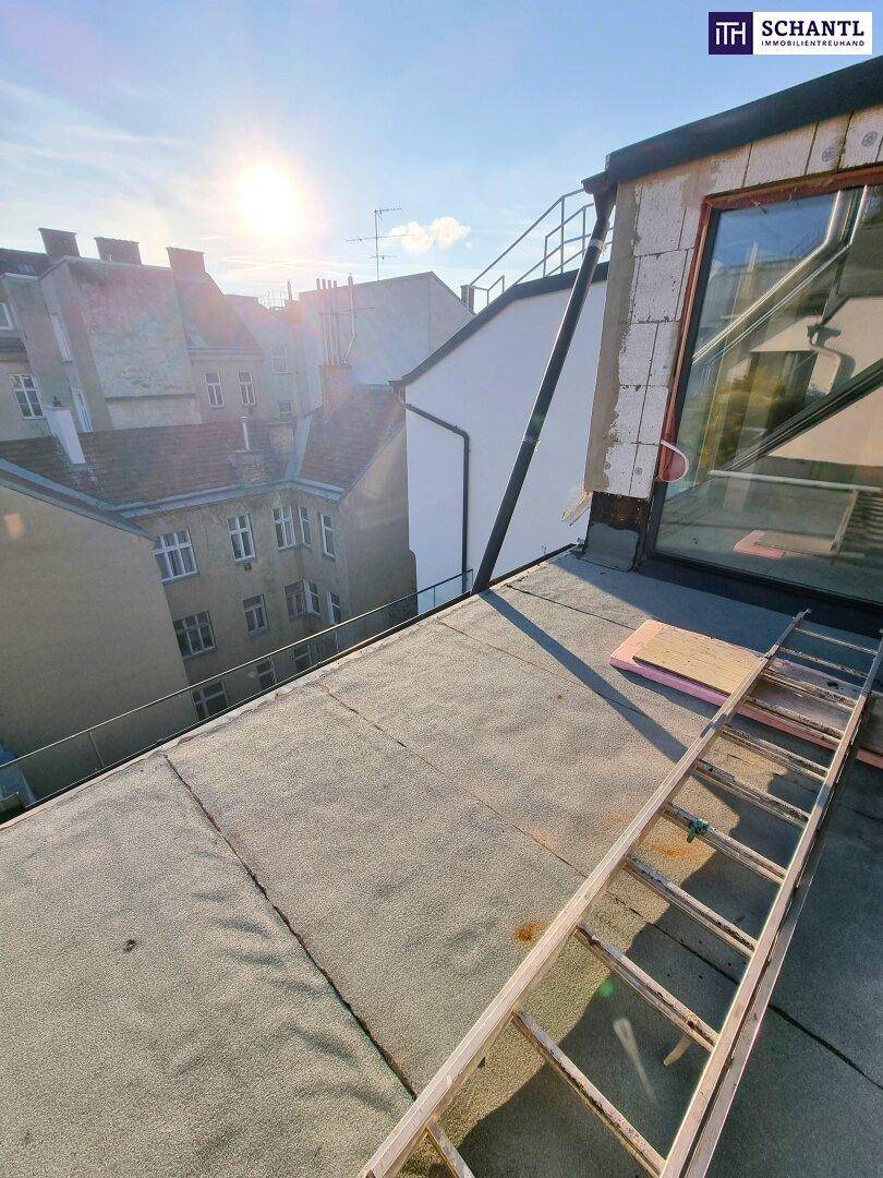 Dachfläche eines Gebäudes mit Leiter und Blick auf umliegende Dächer und den Himmel.
