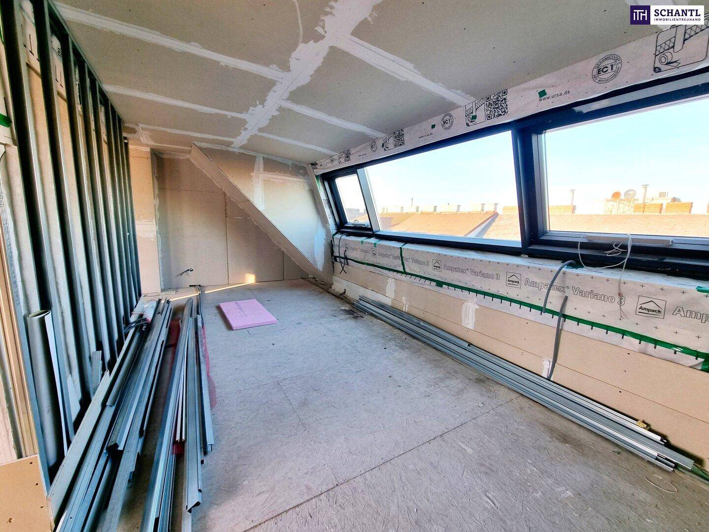 Dachgeschossraum im Rohbau mit schrägen Wänden und breiten Dachfenstern, bereit für den Ausbau.