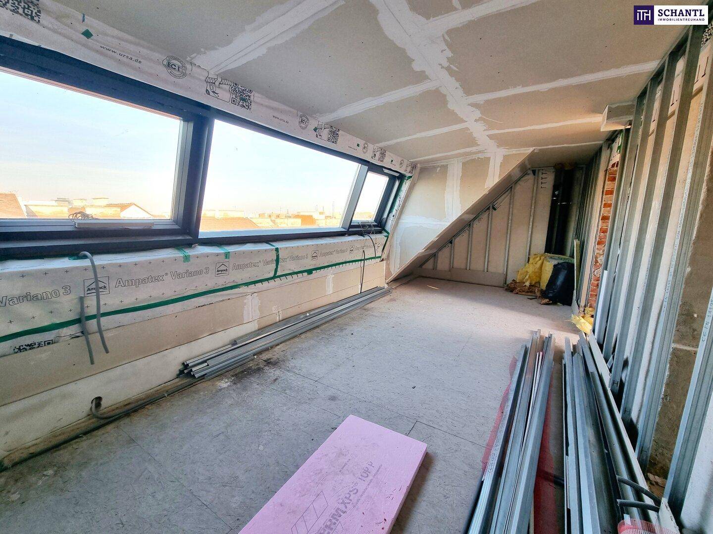 Dachgeschossraum im Rohbau mit schrägen Wänden und Dachfenstern, bereit für den Innenausbau.