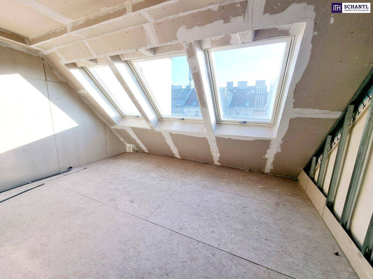 Dachgeschossraum im Rohbau mit schrägen Wänden und zwei großen Dachfenstern.