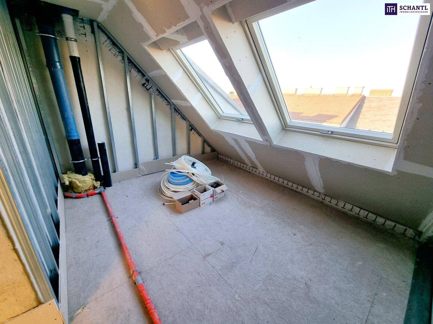 Dachgeschossraum im Rohbau mit schrägen Wänden, Dachfenster und sichtbaren Installationen.
