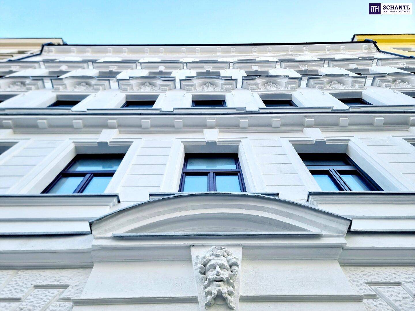 Detailansicht einer historischen Fassade mit aufwendigen Stuckverzierungen und blauen Fenstern.