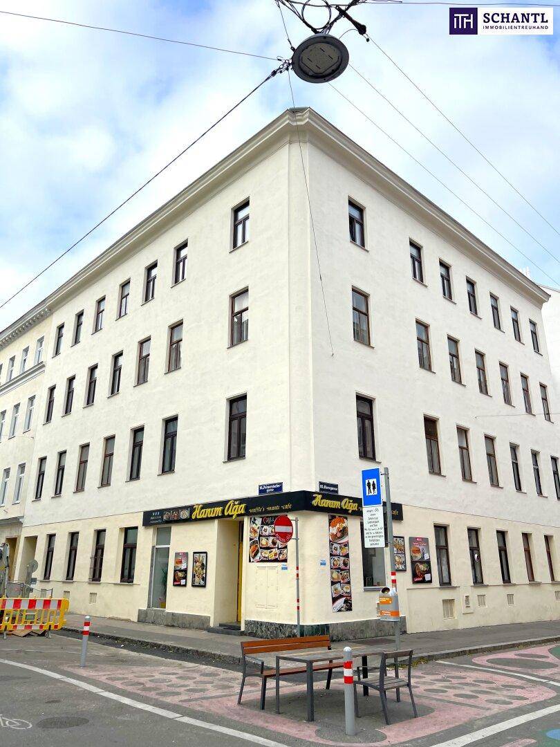 Eckgebäude mit weißer Fassade und vielen Fenstern an einer städtischen Kreuzung.