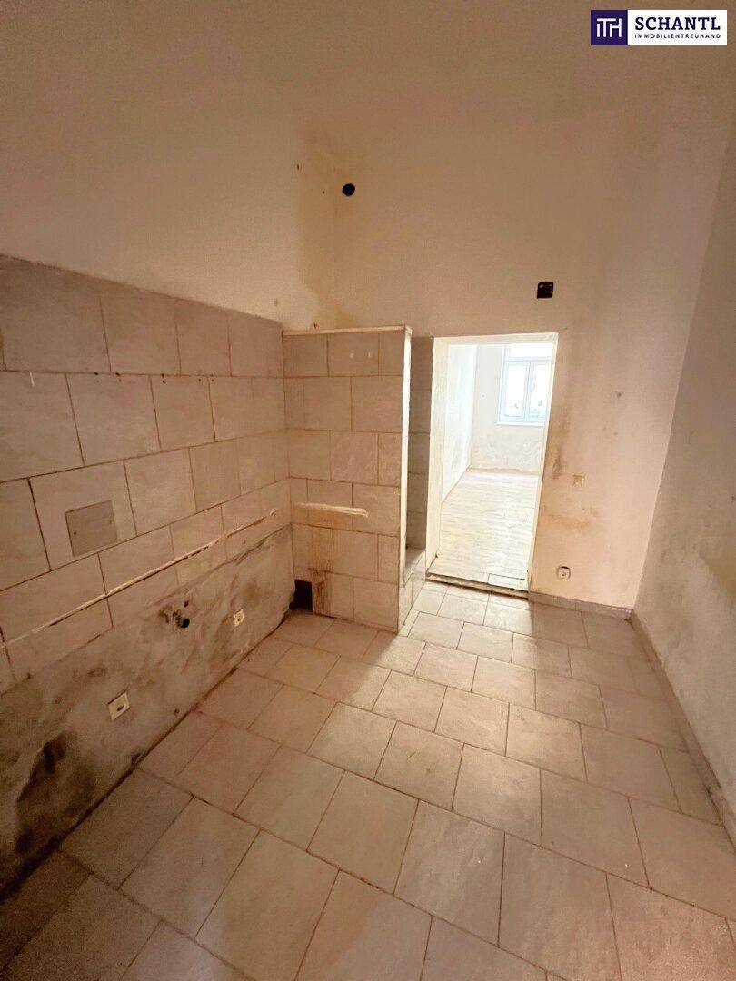 Raum mit Fliesenboden und teilweise gefliesten Wänden, der für eine Küche oder einen Hauswirtschaftsraum vorbereitet ist.