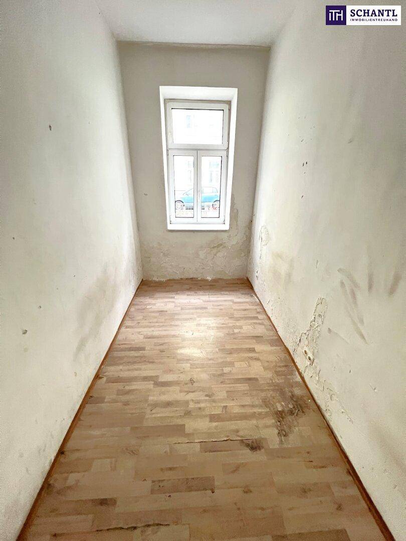 Schmaler, leerer Raum mit Holzboden und einem Fenster, der Renovierungsbedarf aufweist.