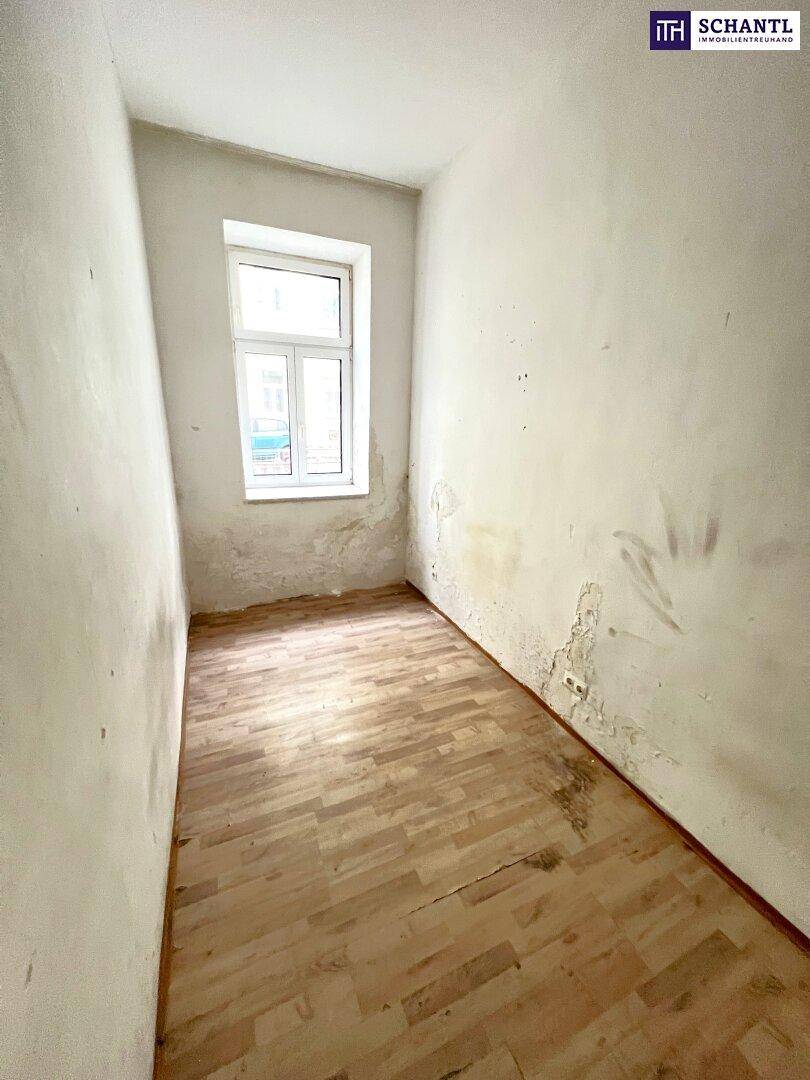 Leerer Raum mit Holzboden und einem Fenster, das auf die Straße blickt, mit Renovierungsbedarf.