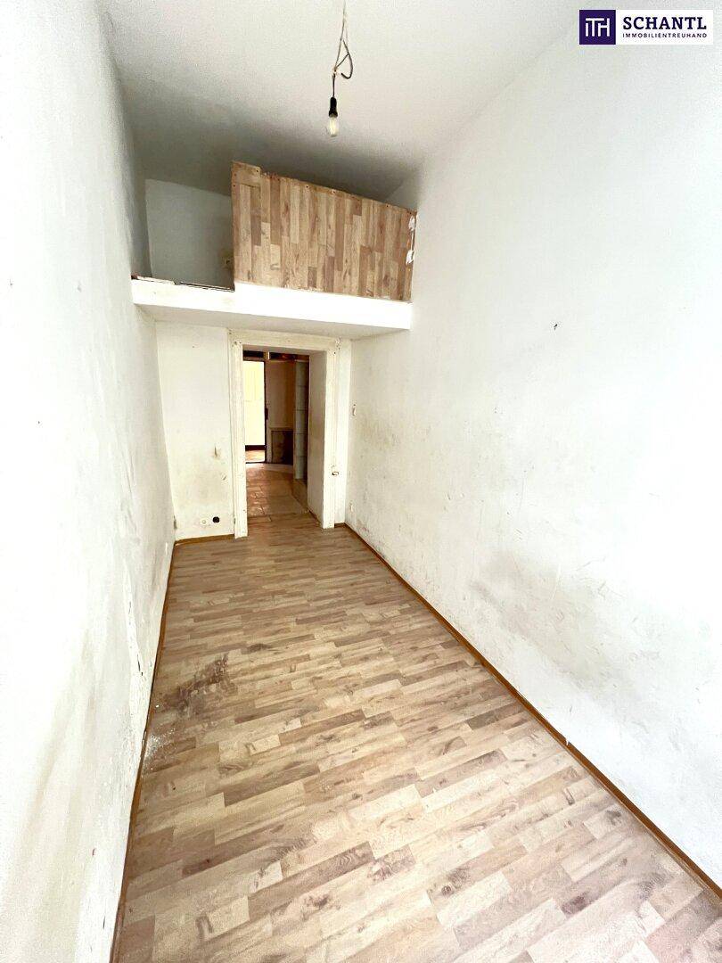Langer, leerer Raum mit Holzboden und einer kleinen Holzkonstruktion im oberen Bereich, bereit zur Renovierung.