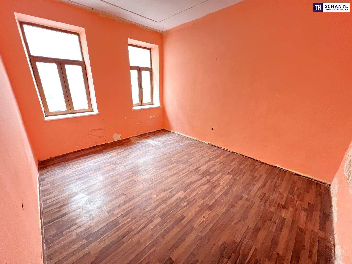 Leerer Raum mit orangefarbenen Wänden, Holzboden und zwei Fenstern, der Renovierung bedarf.