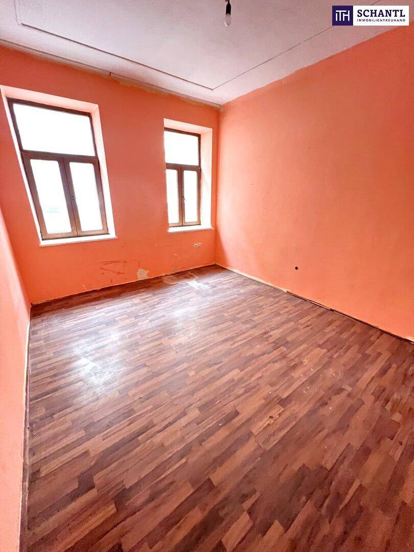 Heller Raum mit abgenutztem Holzboden und leuchtend orangefarbenen Wänden, bereit zur Renovierung.