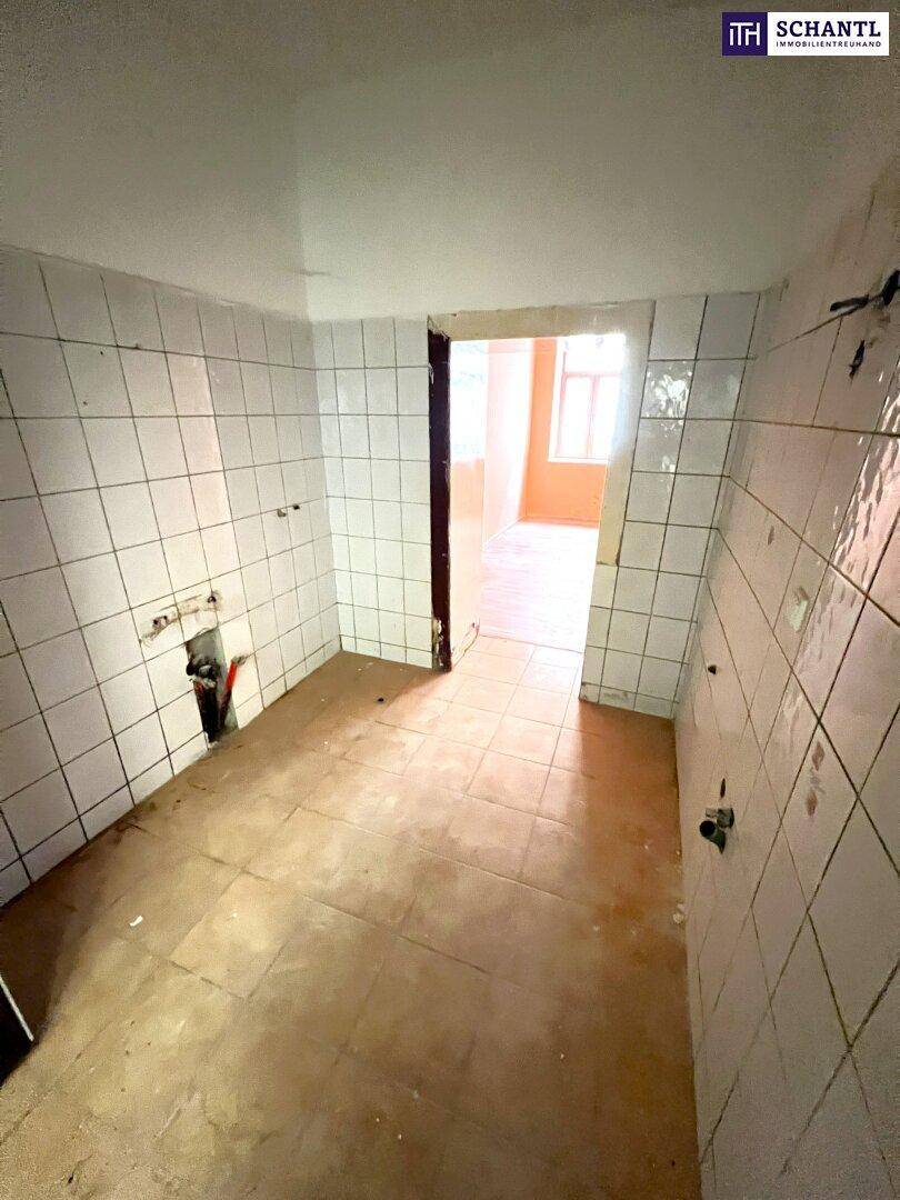 Leere Küche mit weißen Fliesen an den Wänden und braunem Fliesenboden, bereit für den Einbau.
