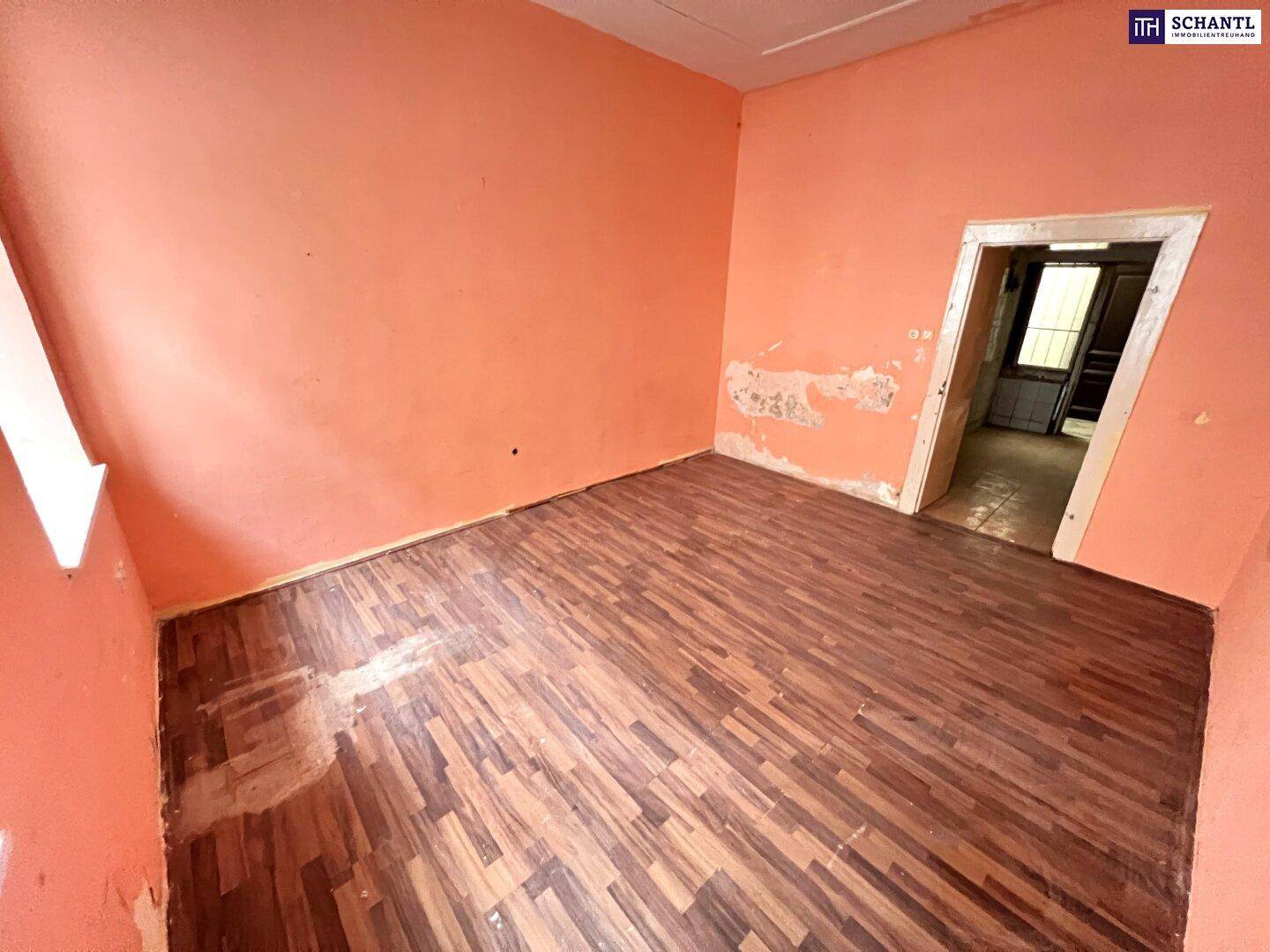 Wohnraum mit orangefarbenen Wänden, Holzboden und einem Durchgang zu einem weiteren Zimmer.