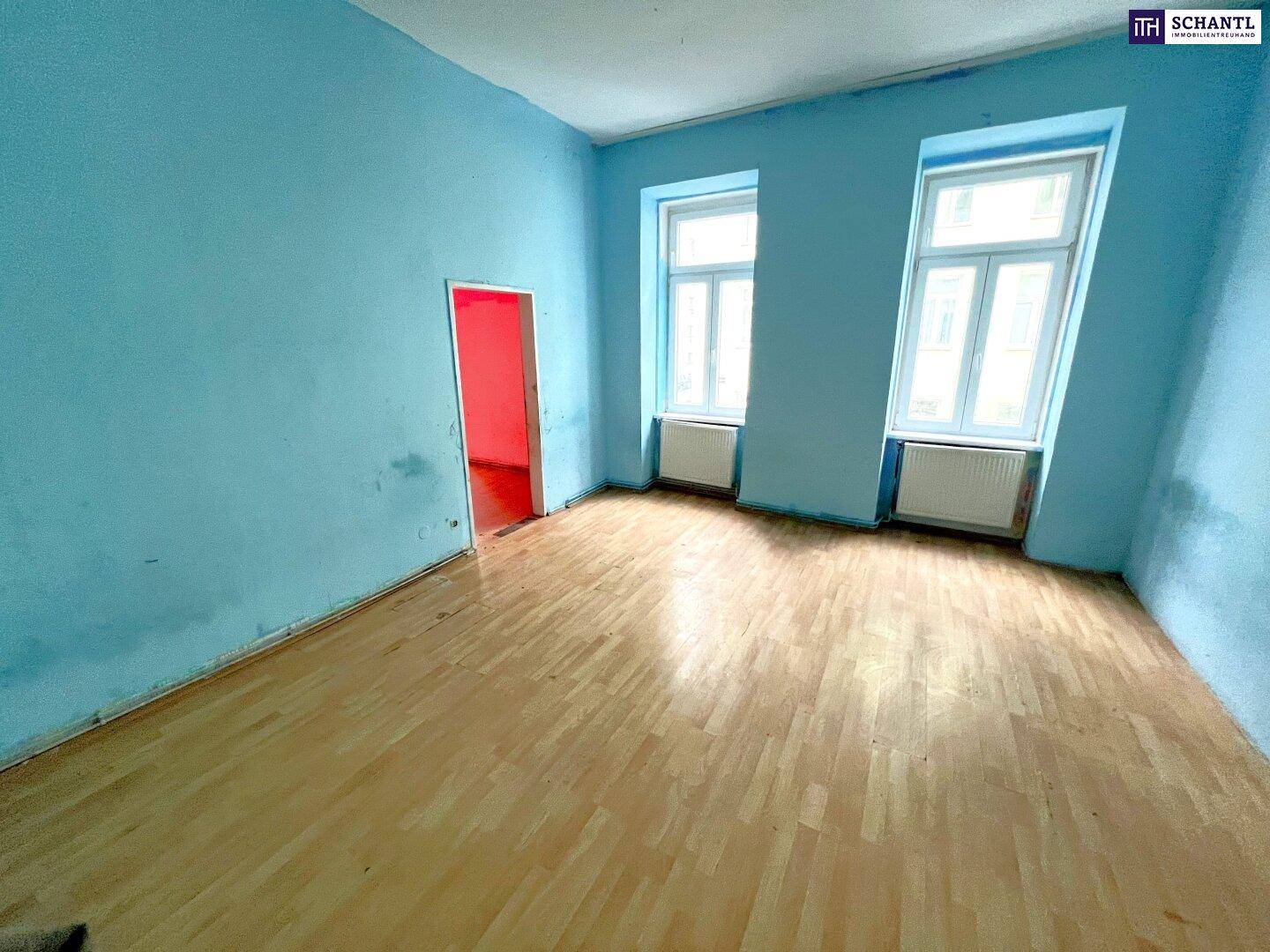 Geräumiger Raum mit hellblauen Wänden, Holzfußboden und zwei Fenstern, bereit zur Renovierung.