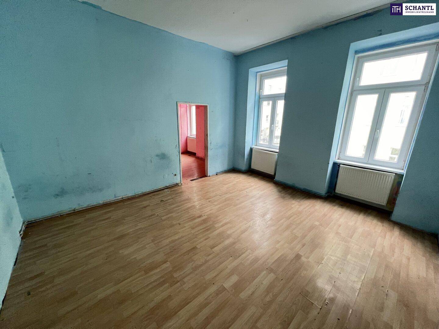 Geräumiger Raum mit hellblauen Wänden, Holzfußboden und zwei Fenstern, bereit zur Renovierung.