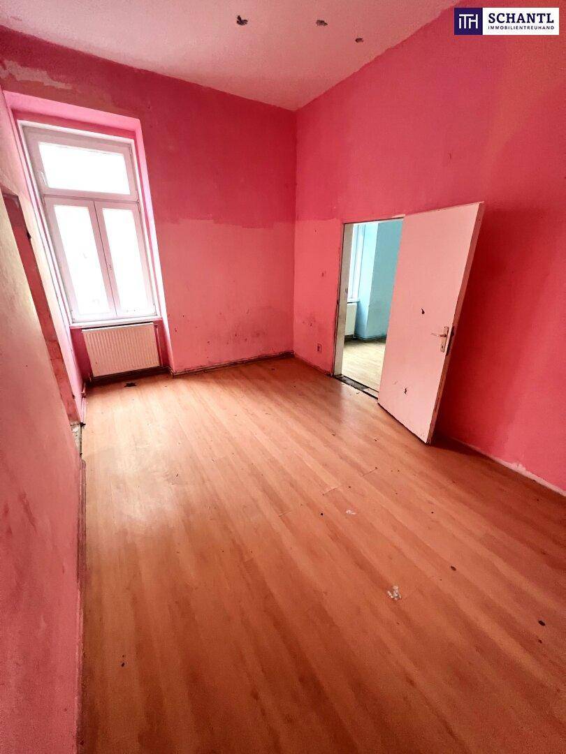 Leerer Raum mit rosa Wänden, Holzfußboden und einem Fenster, bereit zur Renovierung.