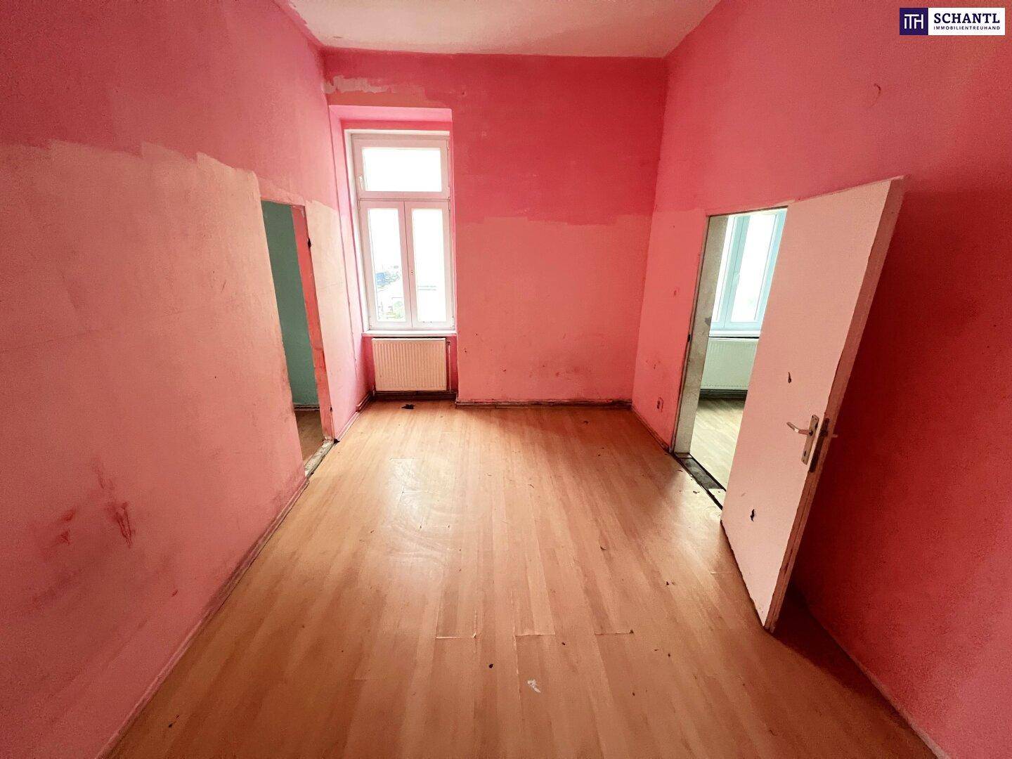 Leerer Raum mit rosa Wänden, Holzfußboden und einem Fenster, bereit zur Renovierung.