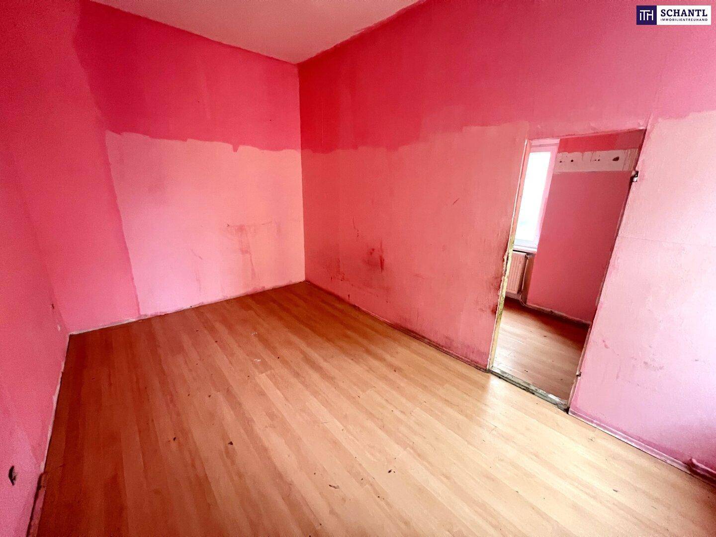 Leerer Raum mit rosa Wänden, Holzfußboden und einem Fenster, bereit zur Renovierung.