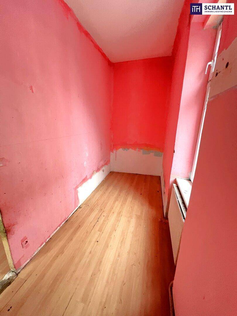 Schmaler Raum mit rosa Wänden, Holzfußboden und einem Fenster, bereit zur Renovierung.