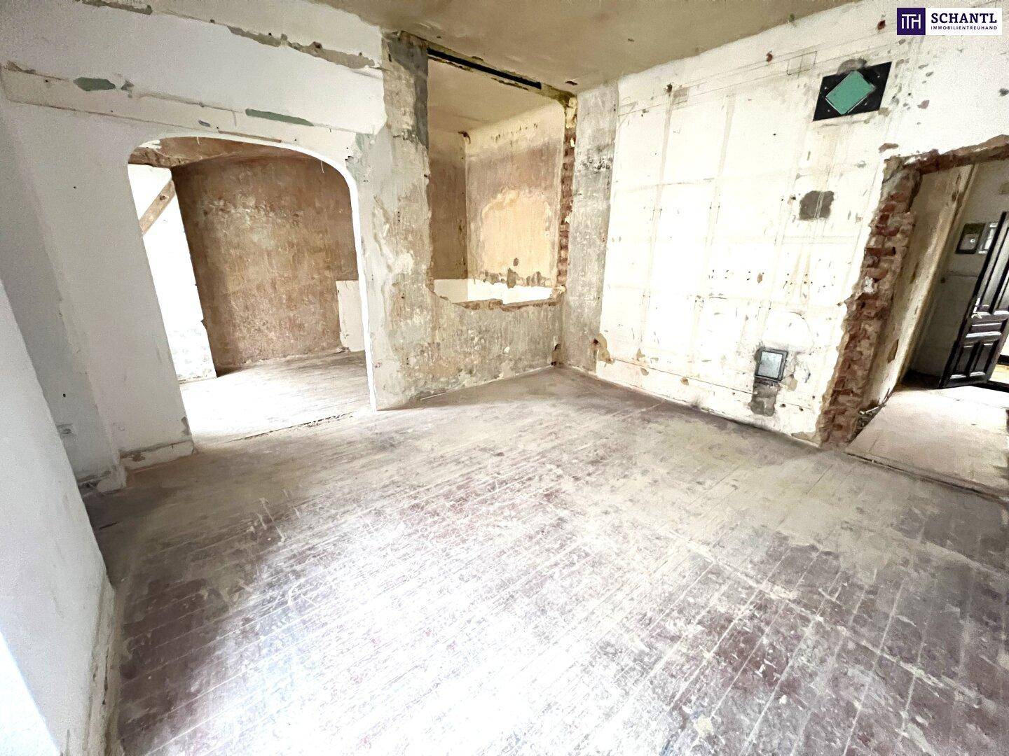 Renovierungsbedürftiger Innenraum mit freigelegten Ziegeln und abgenutztem Holzboden, viel Potenzial.