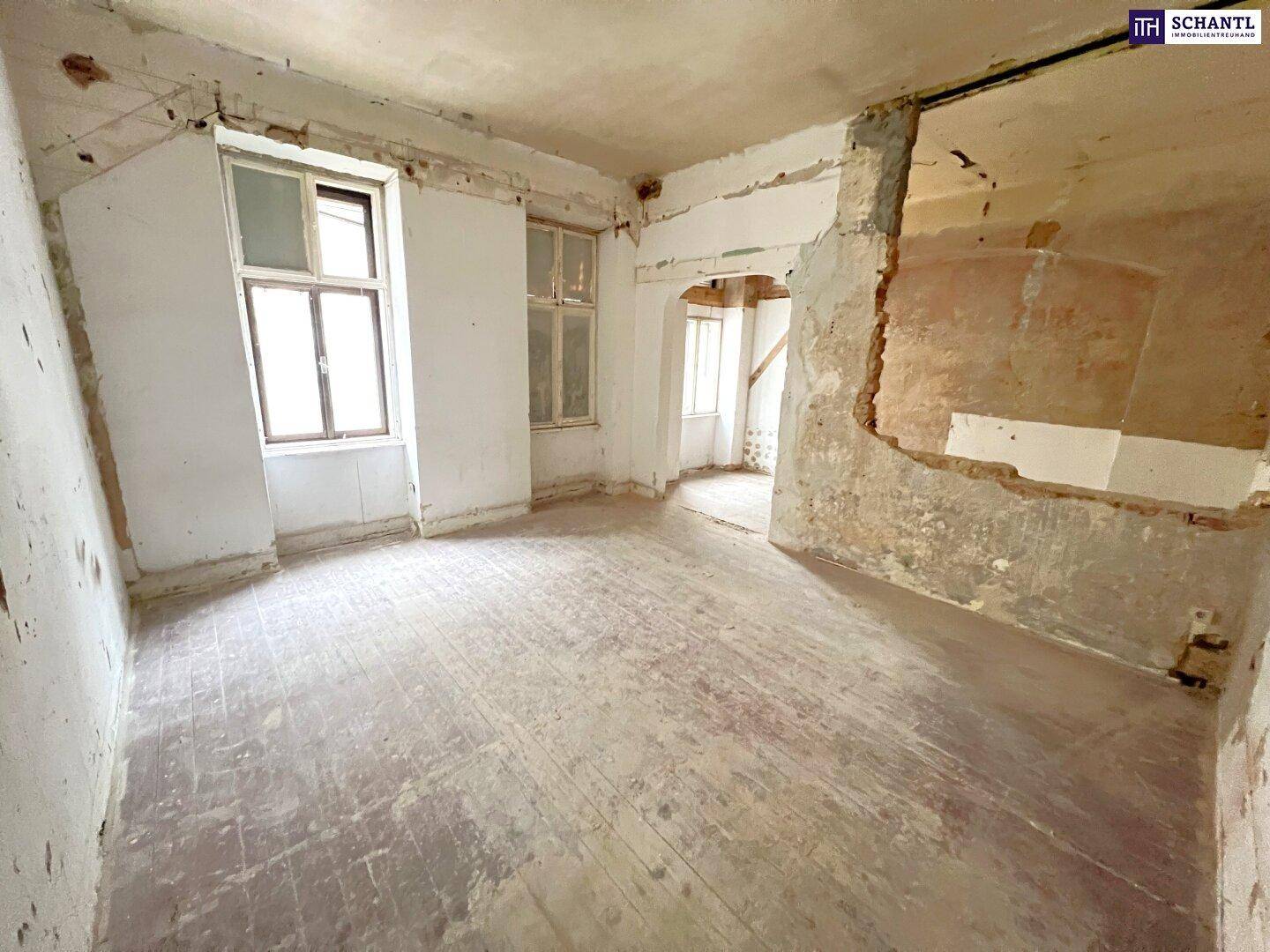 Innenraum in Abrisszustand mit freigelegten Wänden und altem Holzboden, bereit zur Renovierung.