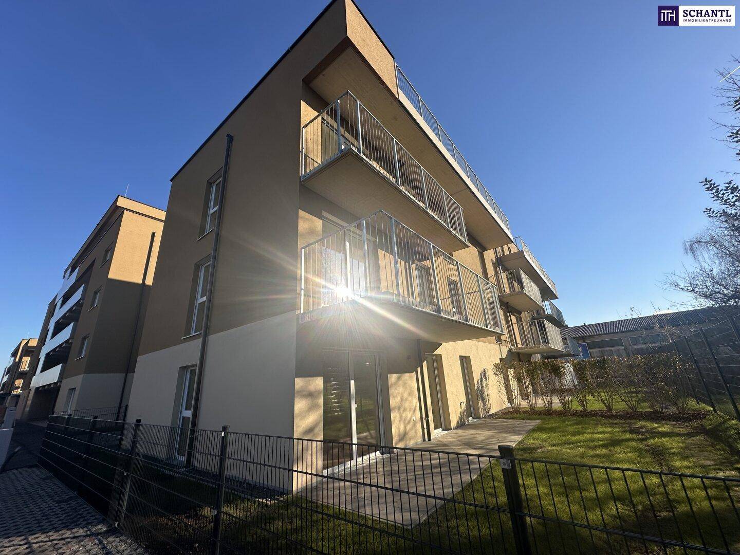 Modernes Apartmentgebäude mit privaten Gärten im Erdgeschoss und Balkonen bei Sonnenschein.
