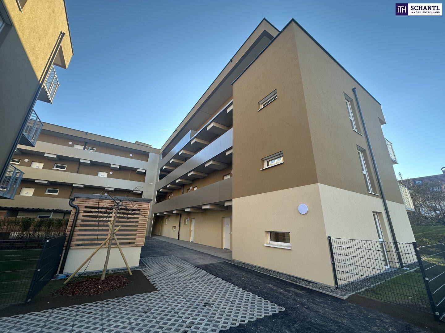 Modernes Apartmentgebäude mit gepflastertem Zugangsweg und umliegenden Grünflächen.