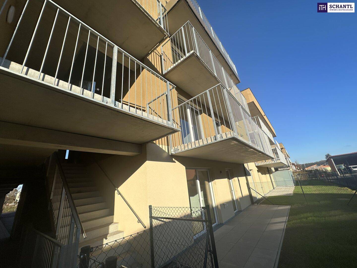 Modernes Apartmentgebäude mit Außentreppe und kleinen Gärten im Erdgeschoss.