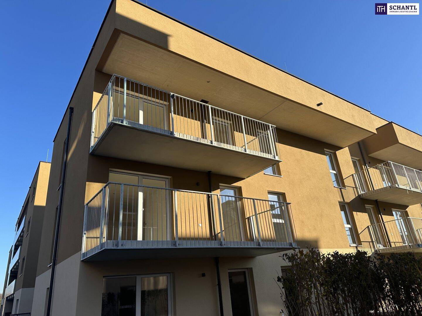 Modernes Apartmentgebäude mit mehreren Balkonen unter strahlend blauem Himmel bei Sonnenschein.