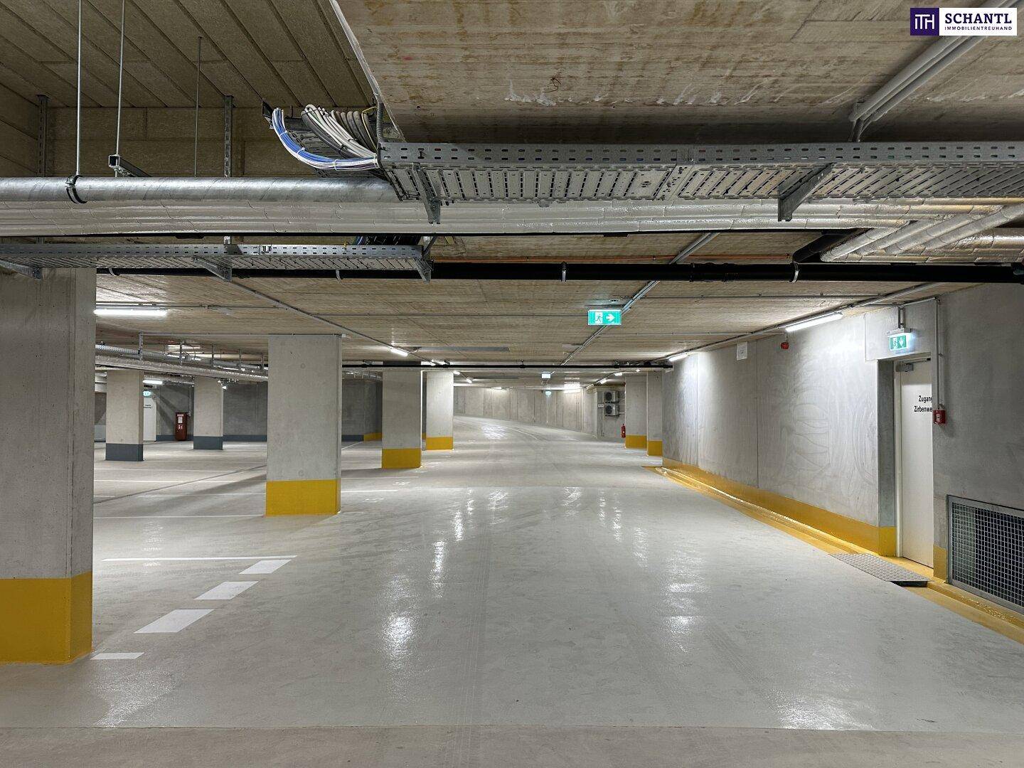 Zufahrtsrampe in eine geräumige Tiefgarage mit Betonwänden und Beleuchtung.