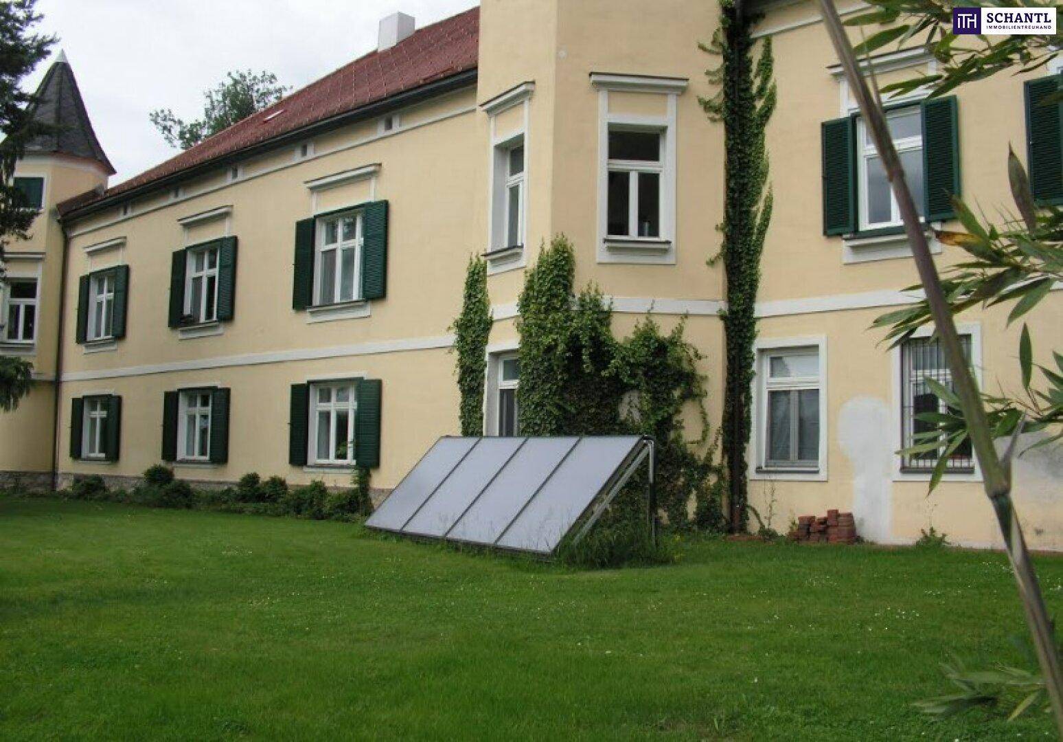 Seitenansicht des historischen Gebäudes mit grünen Fensterläden und einem kleinen Solarpaneel auf dem Rasen.