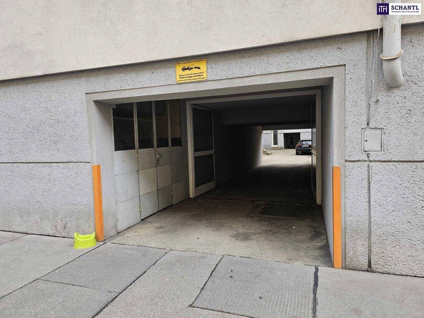 Einfahrt zu einer Tiefgarage mit orangefarbenen Schutzpfosten und einem Hinweisschild.