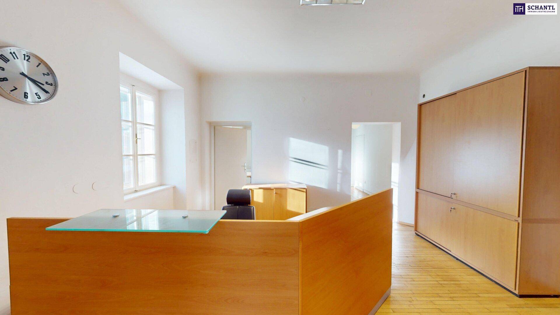 Empfangsbereich mit Holztheke, Glasplatte und Wanduhr, hell durch Fenster und gut gepflegt.