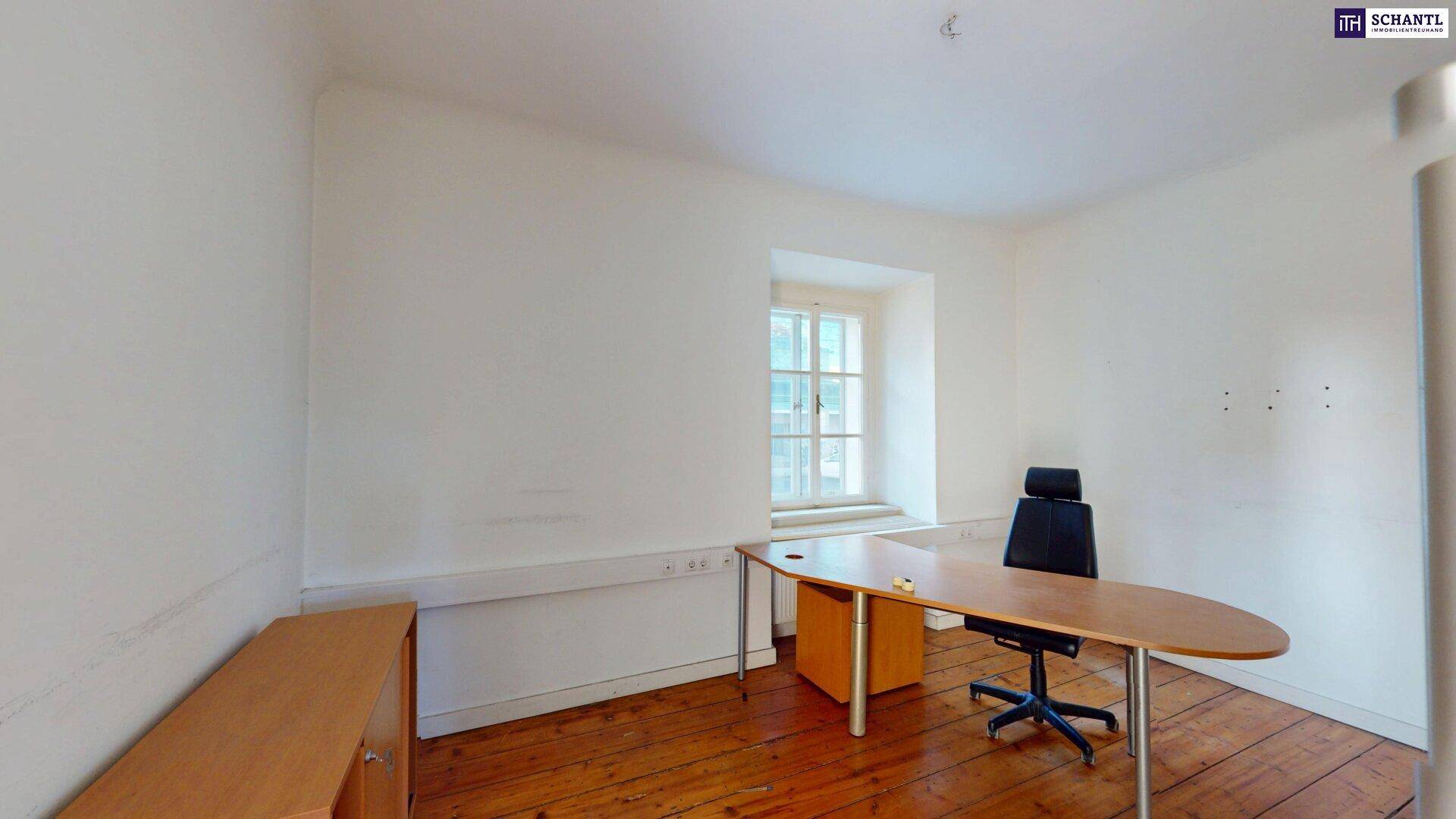 Schlichter Büroraum mit Holzboden, einem Schreibtisch und einem Fenster, das für Helligkeit sorgt.