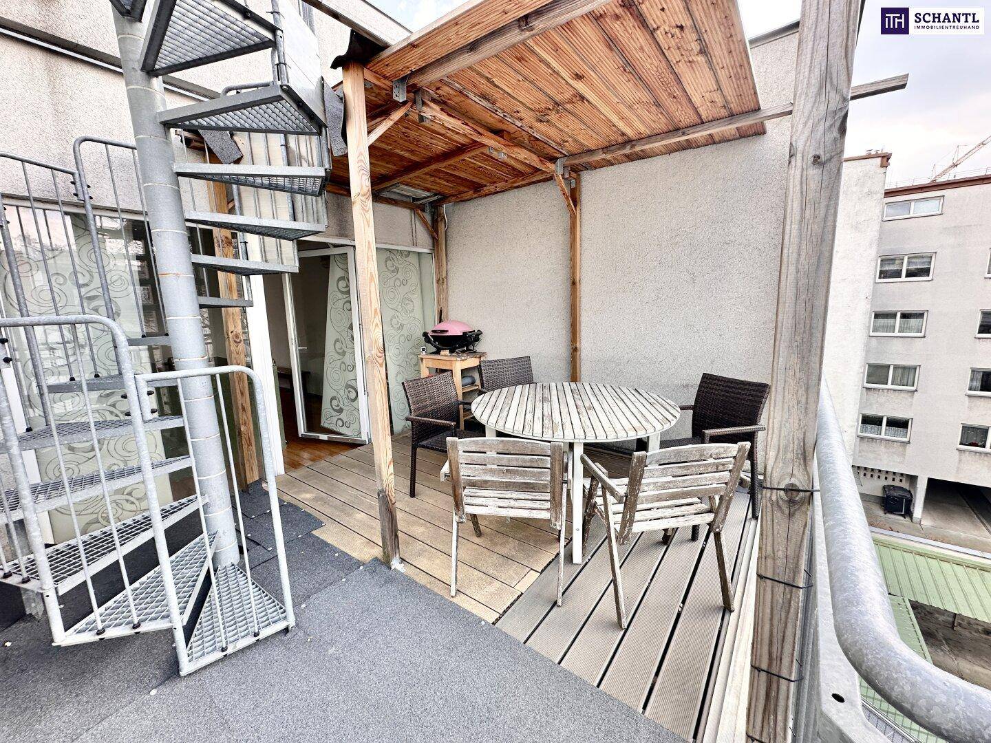 Balkon mit Wendeltreppe, Essbereich im Freien und Blick auf die umliegenden Gebäude.