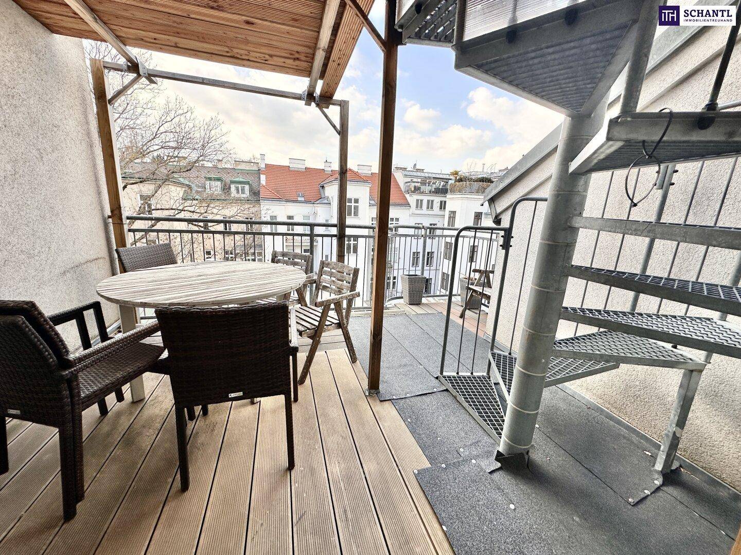 Gemütlicher Balkon mit Holzbelag, Sitzgelegenheiten und Wendeltreppe zur Dachterrasse.
