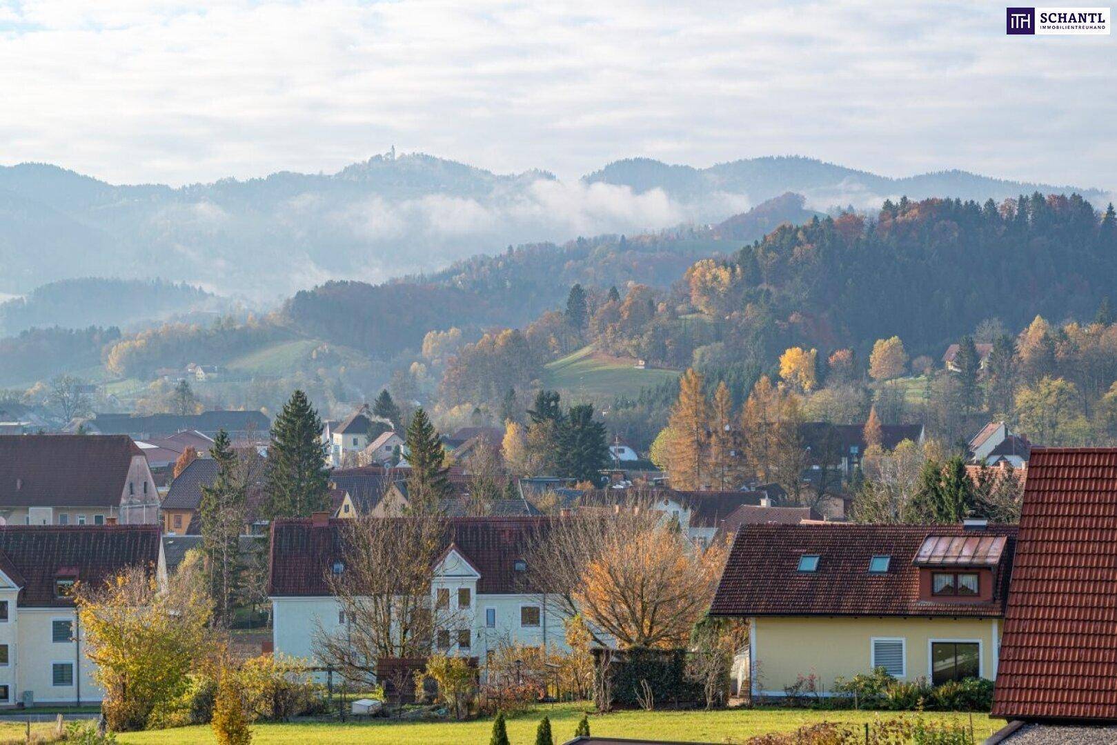 Panoramablick auf eine ländliche Siedlung mit herbstlicher Landschaft und nebligen Hügeln im Hintergrund.