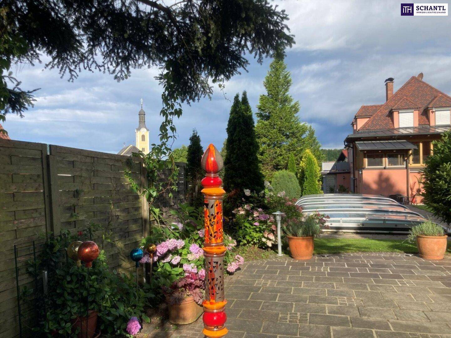 Gepflegter Gartenbereich mit gepflastertem Weg, Blumen und Blick auf eine nahegelegene Kirche.