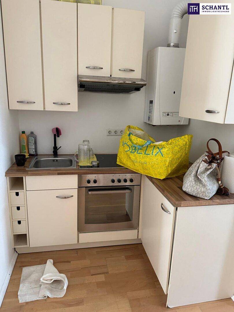 Kompakte Küchenzeile mit hellen Schränken, integriertem Backofen und Holz-Arbeitsplatte.