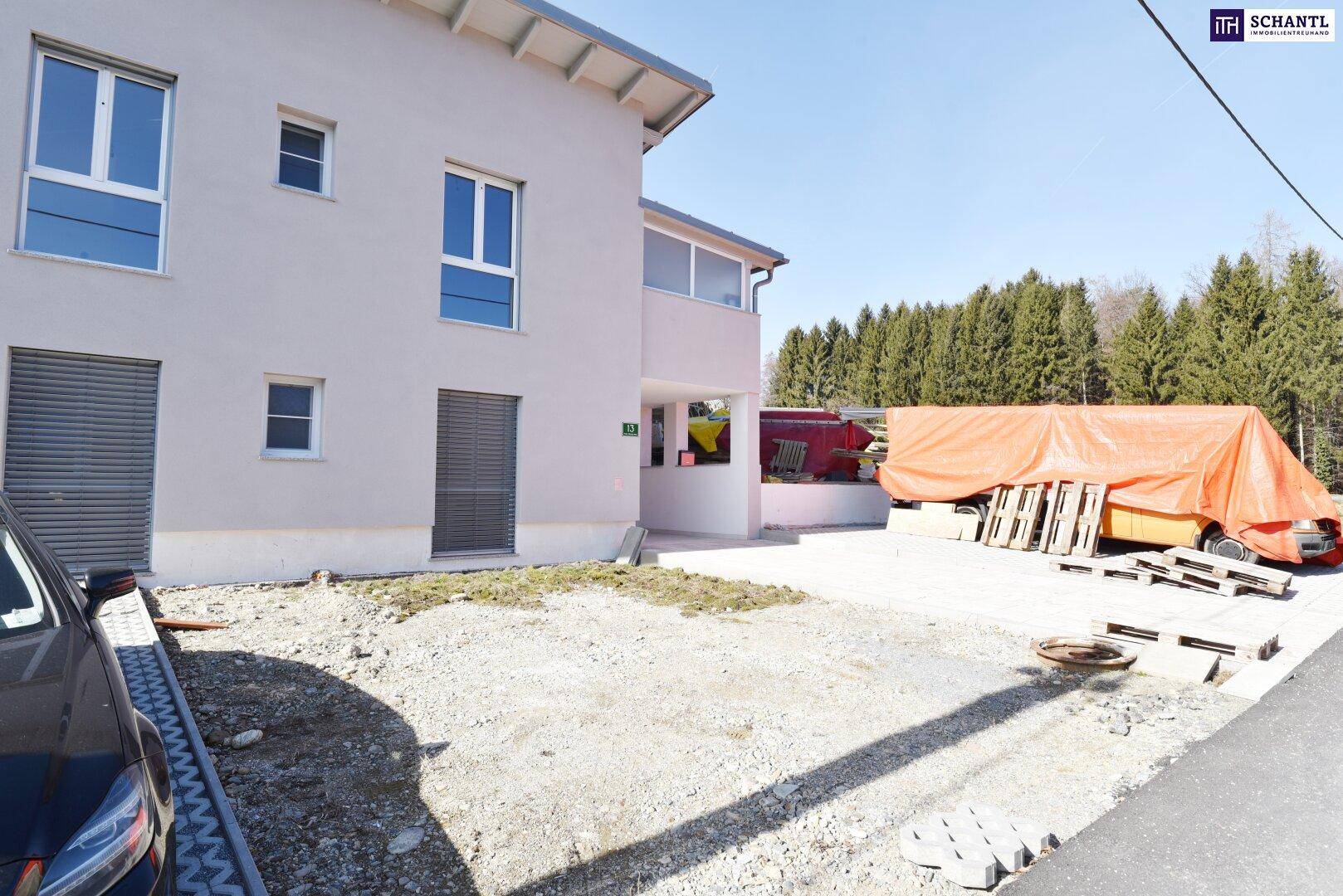 Neubau mit heller Fassade und Baustellenbereich im Vordergrund, umgeben von Bäumen.