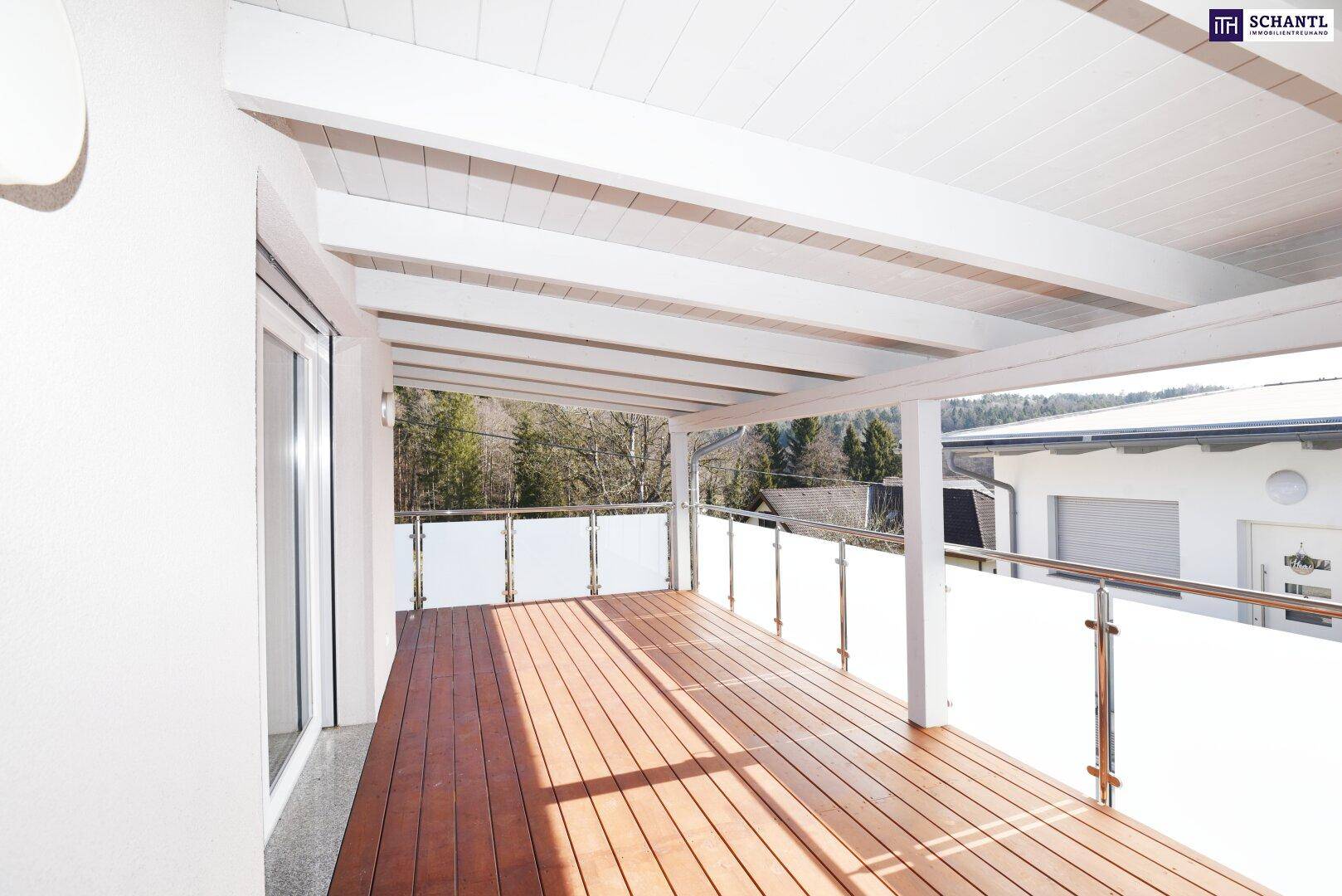 Überdachter Balkon mit Holzboden und Glasgeländer, bietet einen schönen Blick ins Grüne.