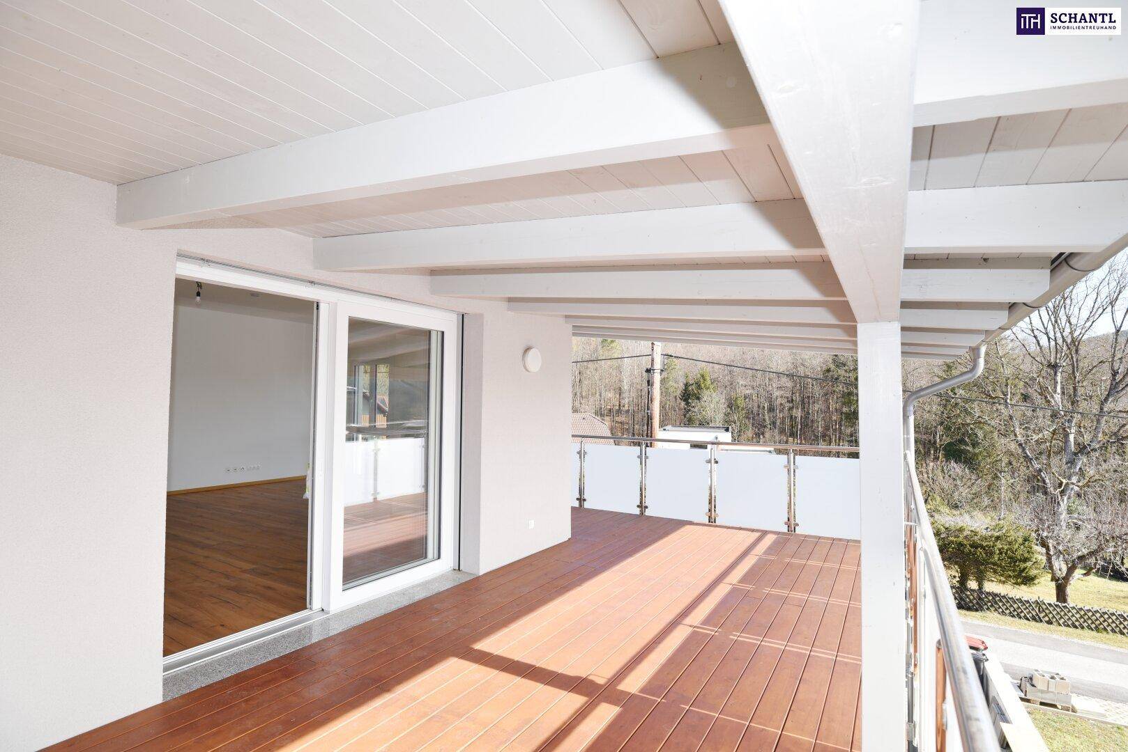 Geräumiger überdachter Balkon mit Holzboden und Glasgeländer, bietet viel Platz im Freien.