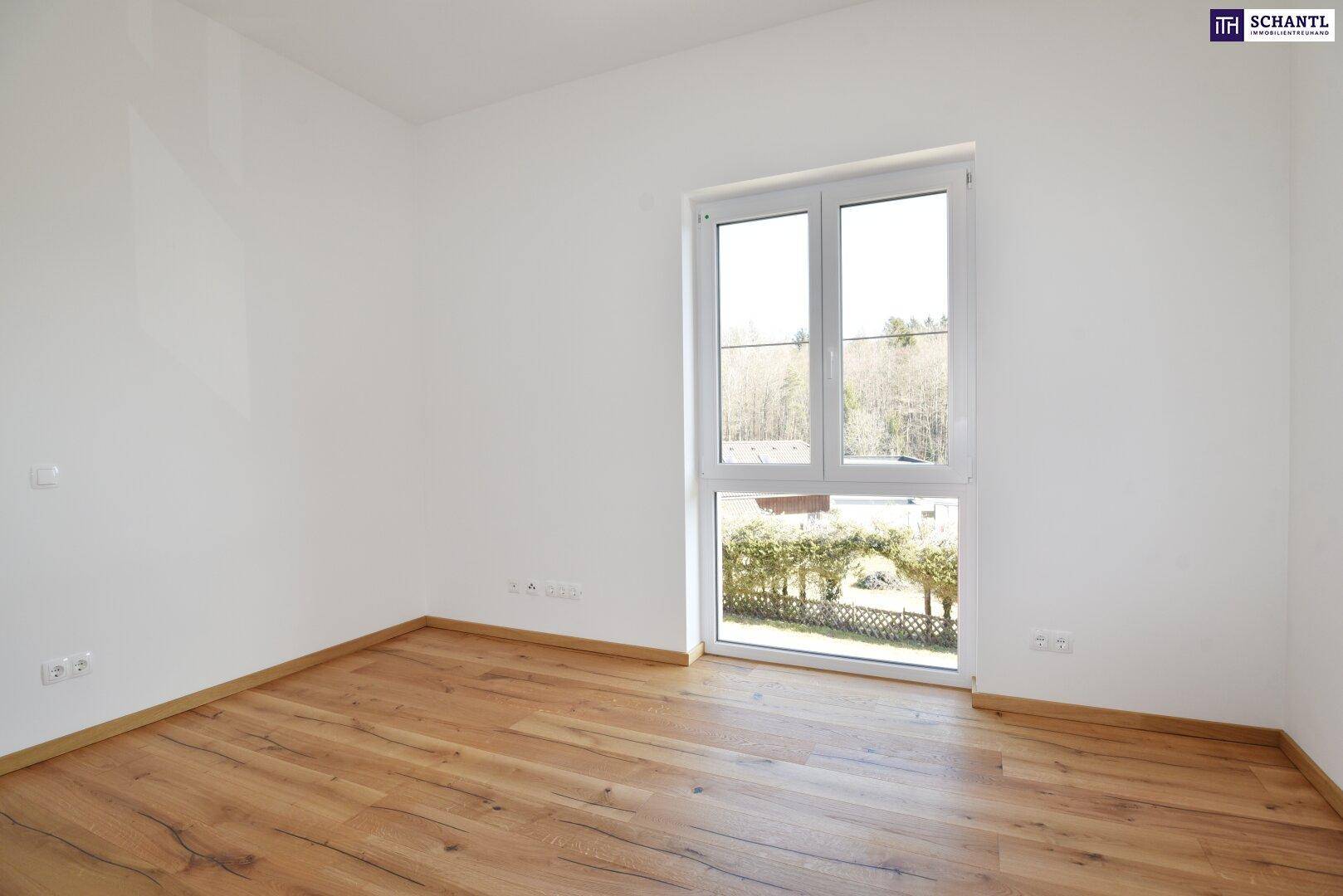 Helles Schlafzimmer mit Holzboden und großem Fenster mit Blick ins Grüne.