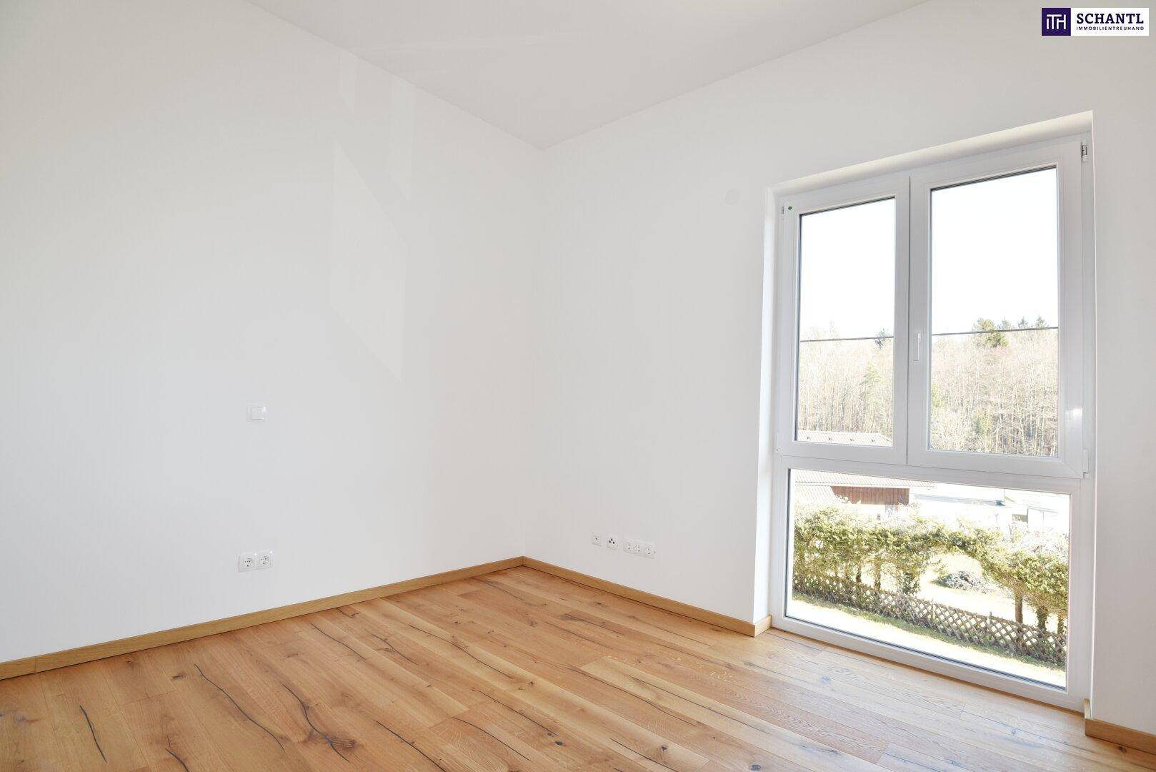 Leeres Schlafzimmer mit Holzboden und großem Fenster, das viel Tageslicht hereinlässt.