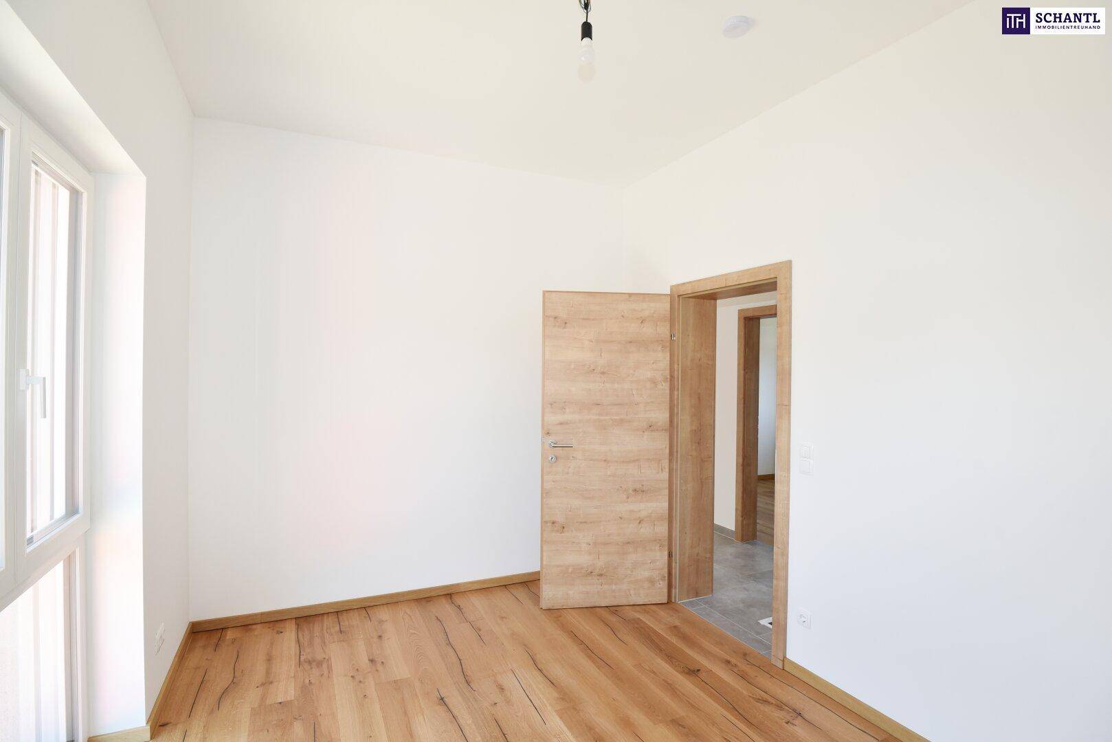 Helles Schlafzimmer mit Holzboden und offener Holztür, die den Zugang zu einem weiteren Raum ermöglicht.