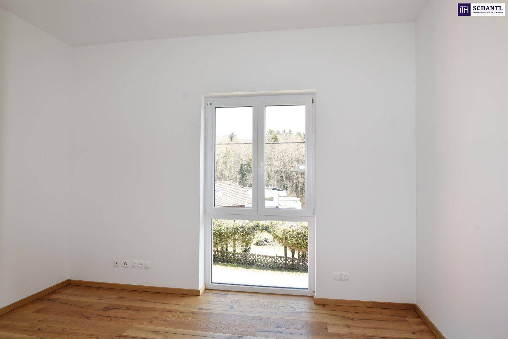 Helles Schlafzimmer mit Holzboden und großem Fenster mit Blick auf die grüne Landschaft.