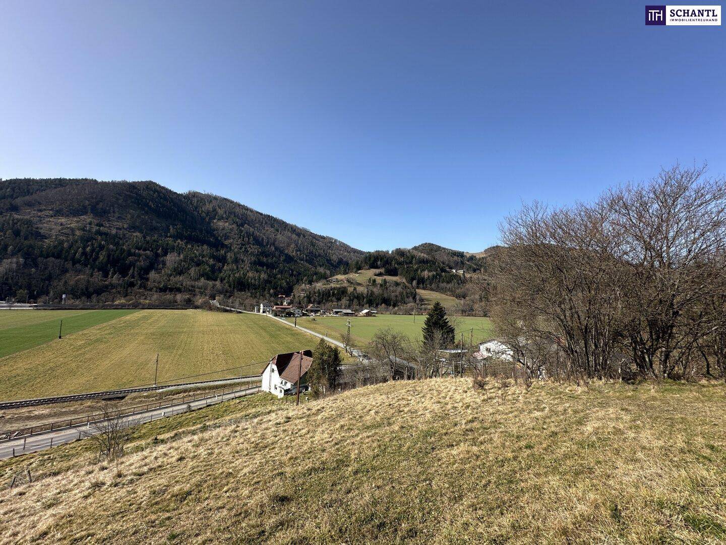 Panoramablick über eine ländliche Landschaft mit Feldern, Bergen und einem einzelnen Haus.