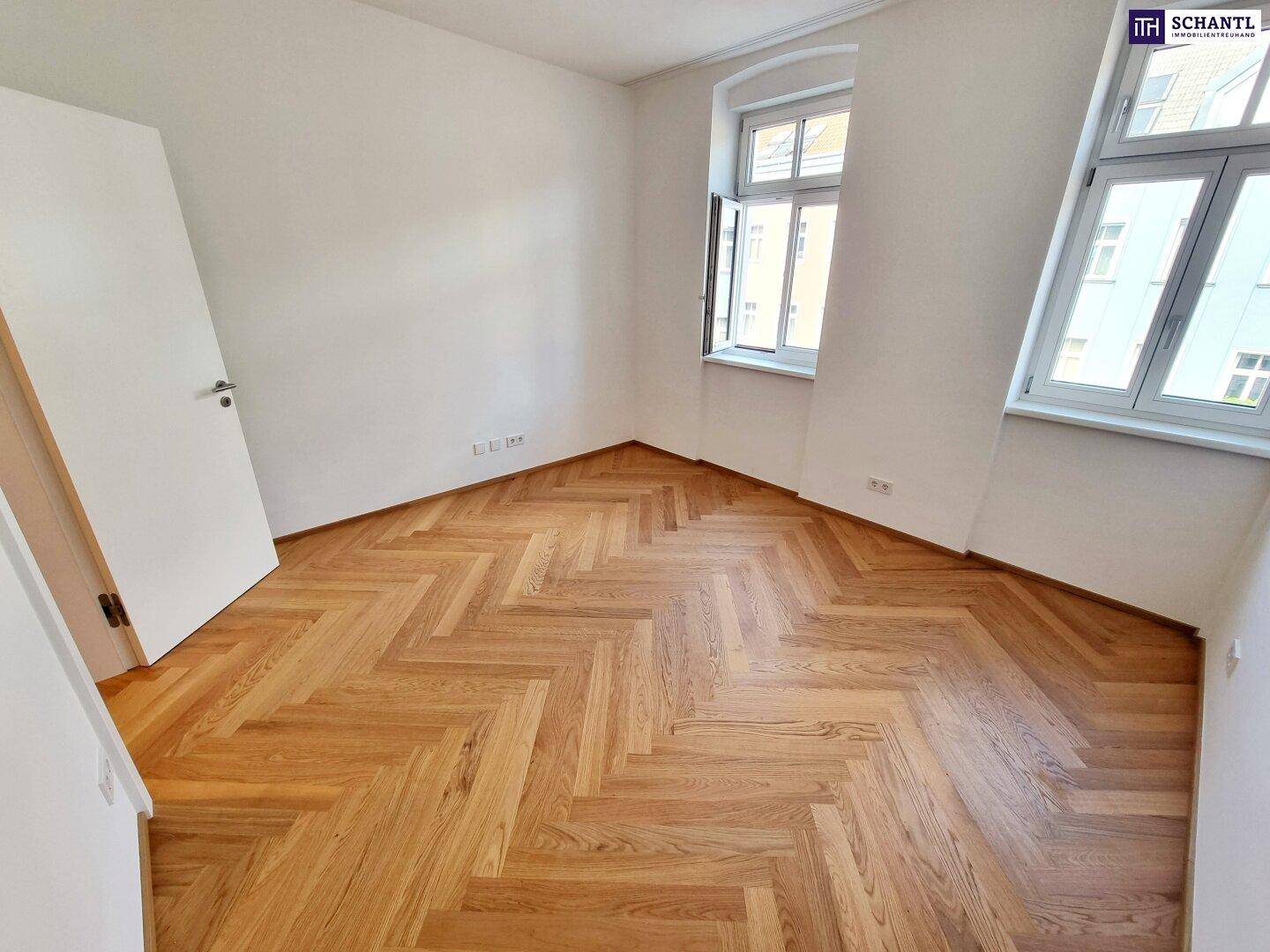 Geräumiges, helles Zimmer mit Fischgrätparkettboden und zwei Fenstern.