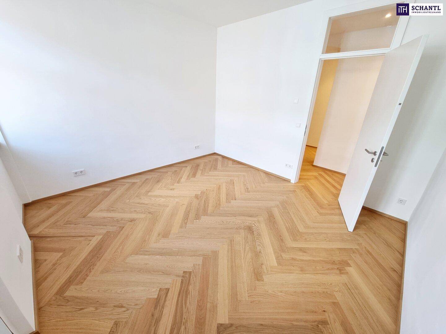 Helles Zimmer mit Fischgrätparkettboden und offener Tür zum Flur.