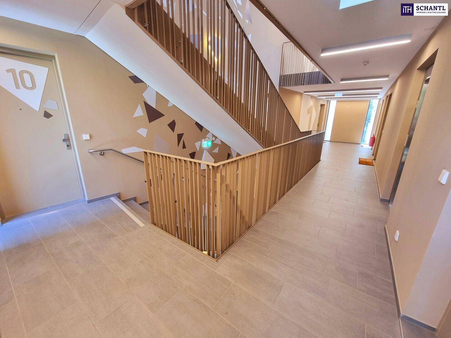 Heller Treppenaufgang und Flur mit modernen Holzgeländern und Fliesenboden in einem Neubau.