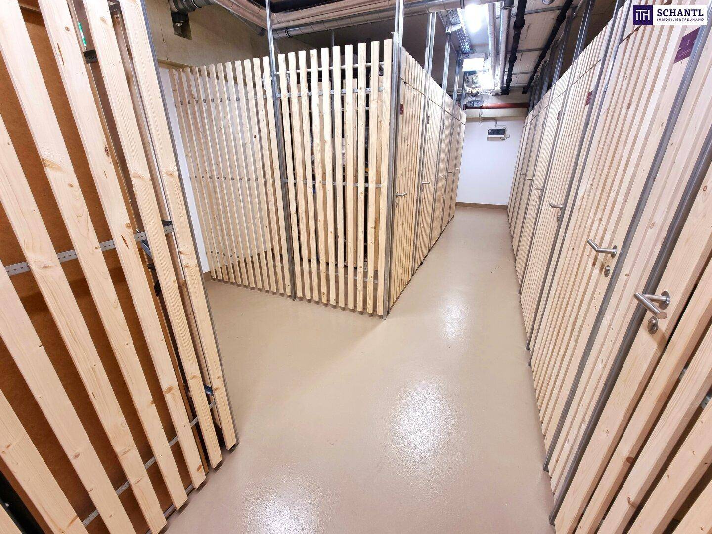 Zahlreiche separate Abstellräume mit Holzlattenwänden in einem Gemeinschaftsbereich eines Neubaus.